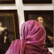 Woman in colorful headscarf in front of somber 17th-century portraits of Dutch elite