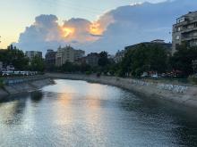 Picture of a river with concrete banks against the background of a cityscape, with the sun breaking through the clouds