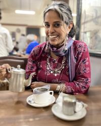 Dr. Anu pouring a cup of chai from a silver tea kettle. 
