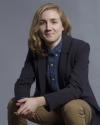 person with long hair wearing blazer and blue shirt looks into camera while smiling