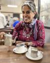 Dr. Anu pouring a cup of chai from a silver tea kettle. 