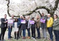A group portrait of Comparative History of Ideas faculty and staff beneath cherry blossoms in the quad, holding signs that say, "question. critique. create."